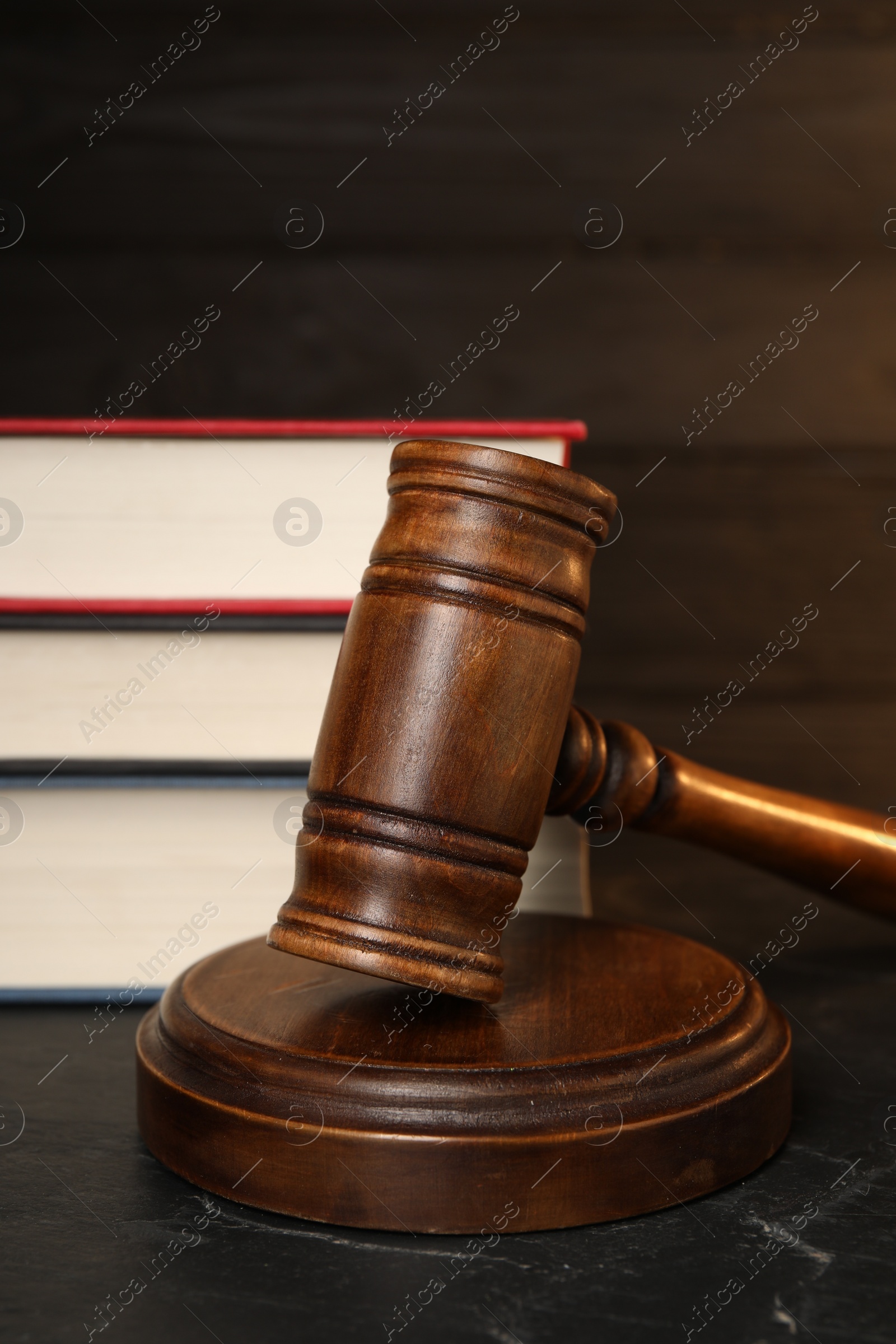 Photo of Wooden gavel and stack of books on dark textured table, closeup