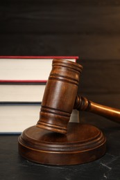 Photo of Wooden gavel and stack of books on dark textured table, closeup