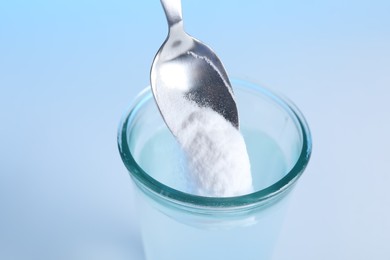 Adding baking soda into glass of water on light blue background, closeup