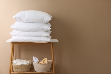 Photo of Stack of soft white pillows and laundry baskets near beige wall. Space for text