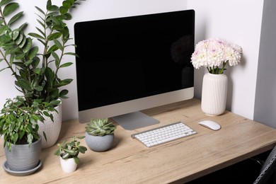 Photo of Comfortable workplace with modern computer, green houseplants and beautiful flowers on wooden table indoors