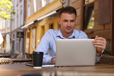 Handsome man working on laptop at table in outdoor cafe