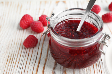 Delicious jam and fresh raspberries on white wooden table, closeup