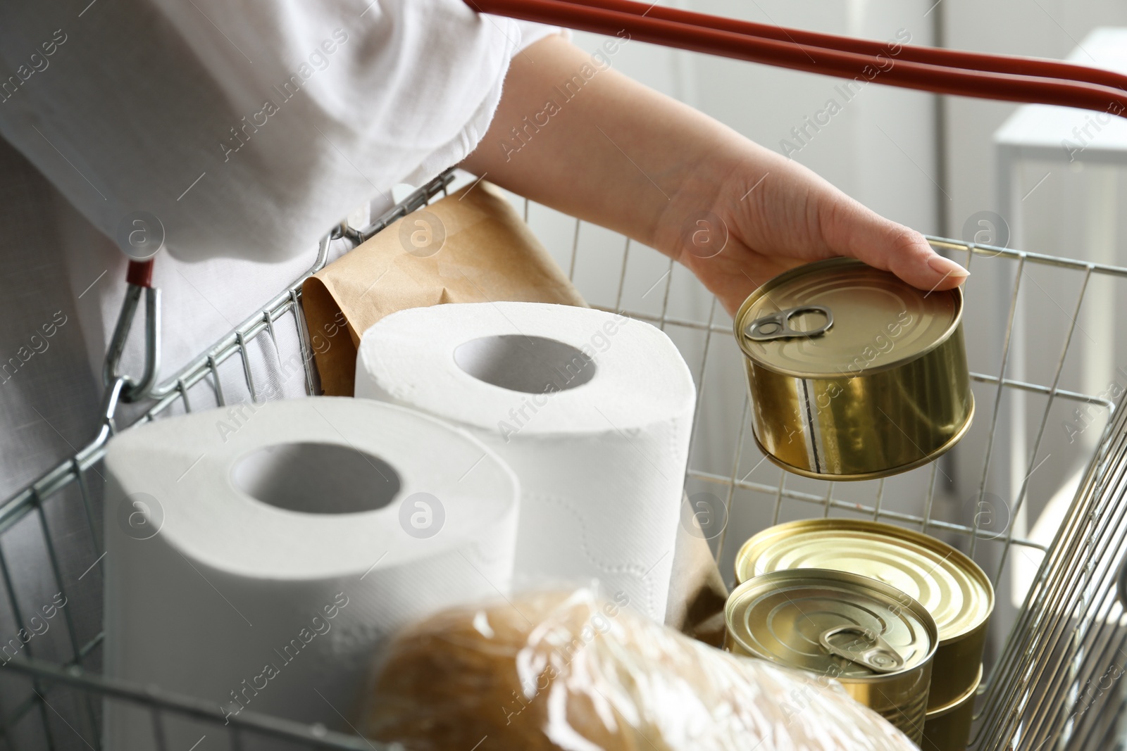 Photo of Woman holding shopping basket with products and toilet paper rolls indoors, closeup. Panic caused by virus