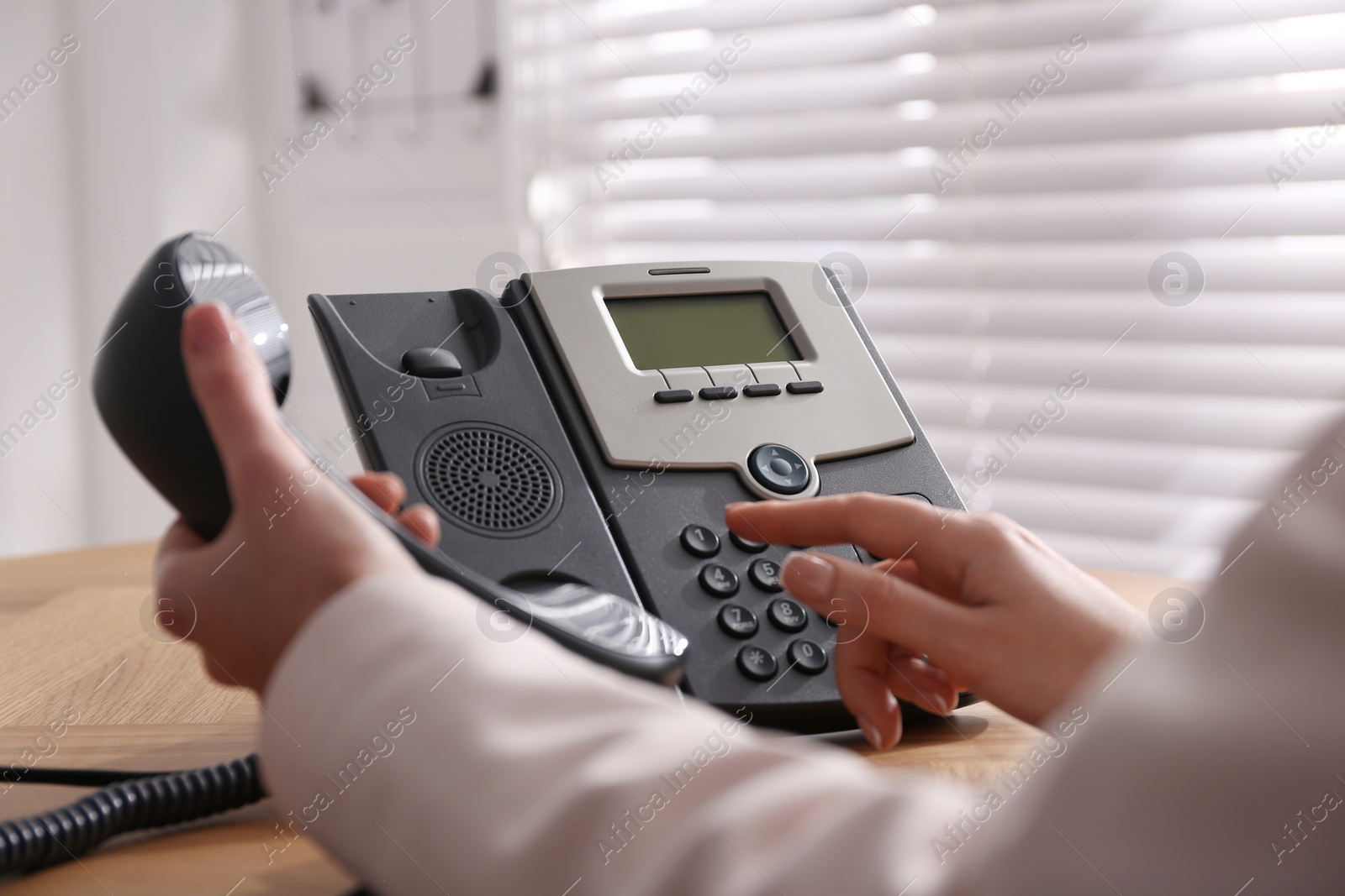 Photo of Woman using desktop telephone at wooden table in office, closeup. Hotline service