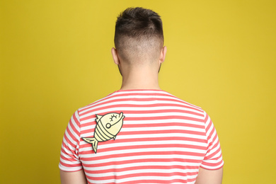 Photo of Man with paper fish on back against yellow background. April fool's day