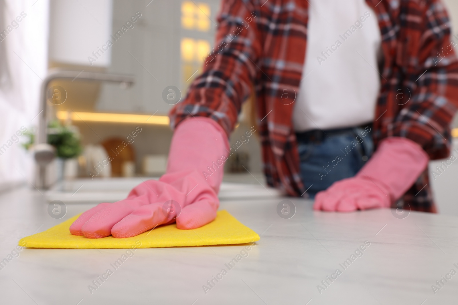 Photo of Woman cleaning white marble table with microfiber cloth in kitchen, closeup