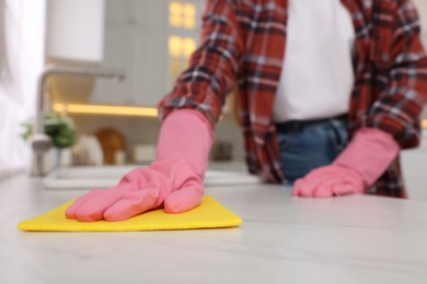 Woman cleaning white marble table with microfiber cloth in kitchen, closeup