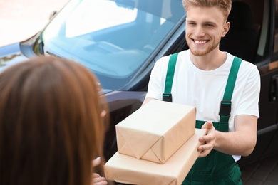 Photo of Young delivery courier giving parcels to customer outdoors