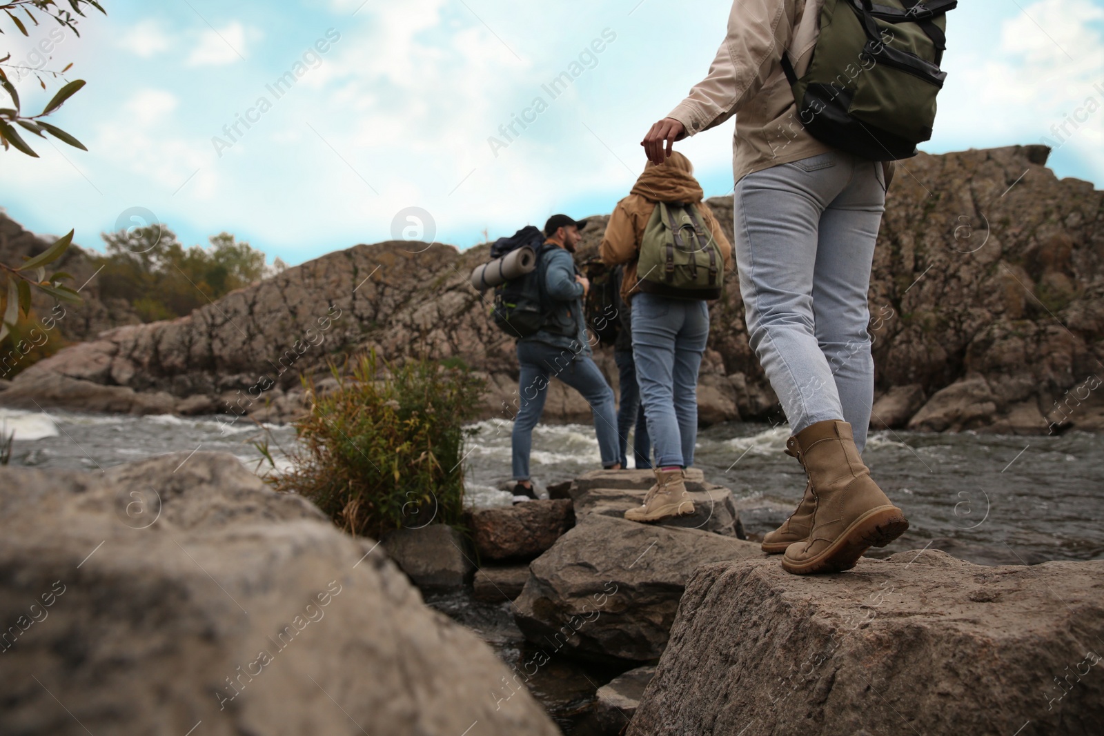 Photo of Group of friends with backpacks crossing mountain river, focus on hiking boots