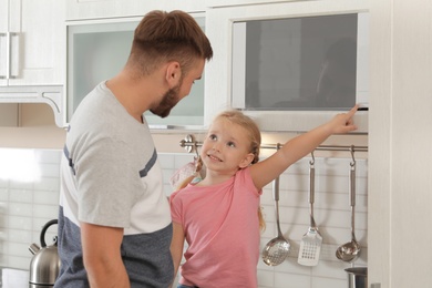 Little daughter and father using microwave oven in kitchen