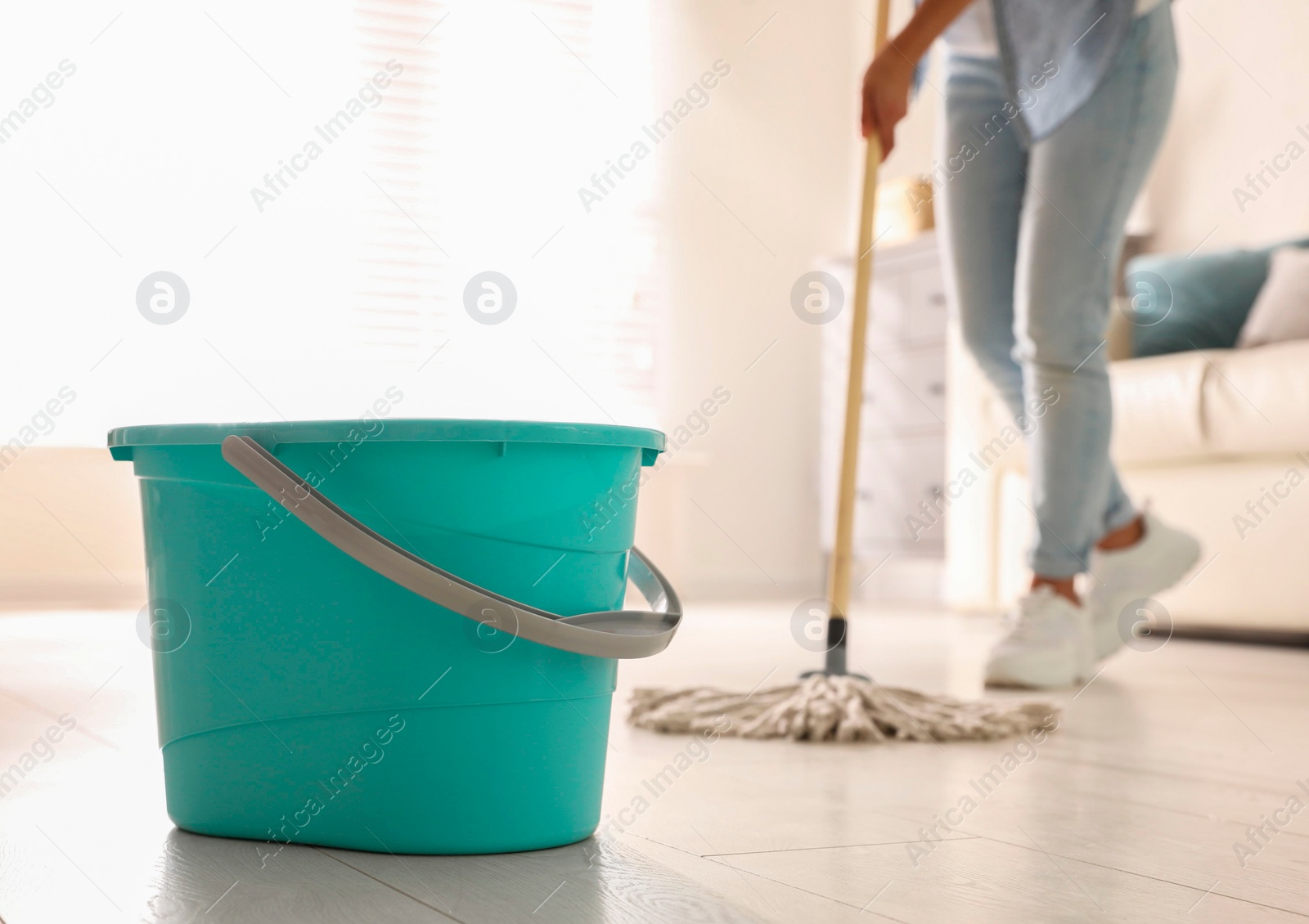 Photo of Plastic bucket and woman mopping floor in living room, closeup. Cleaning supplies