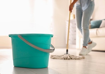 Photo of Plastic bucket and woman mopping floor in living room, closeup. Cleaning supplies