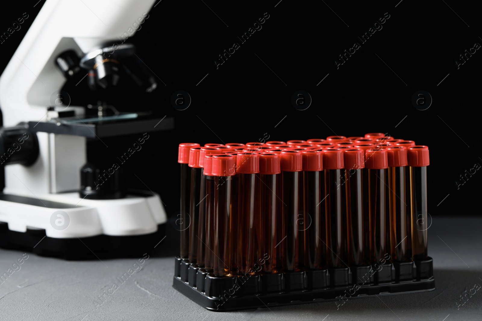 Photo of Test tubes with brown liquid in stand on grey table against black background