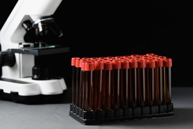 Photo of Test tubes with brown liquid in stand on grey table against black background