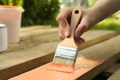 Photo of Woman painting wooden surface with coral dye outdoors, closeup