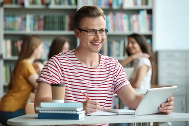 Photo of Young man working on tablet at table in library