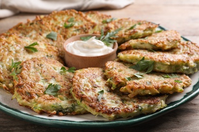 Photo of Delicious zucchini fritters with sour cream served on wooden table, closeup