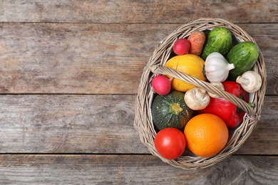 Photo of Basket with ripe fruits and vegetables on wooden table, top view. Space for text