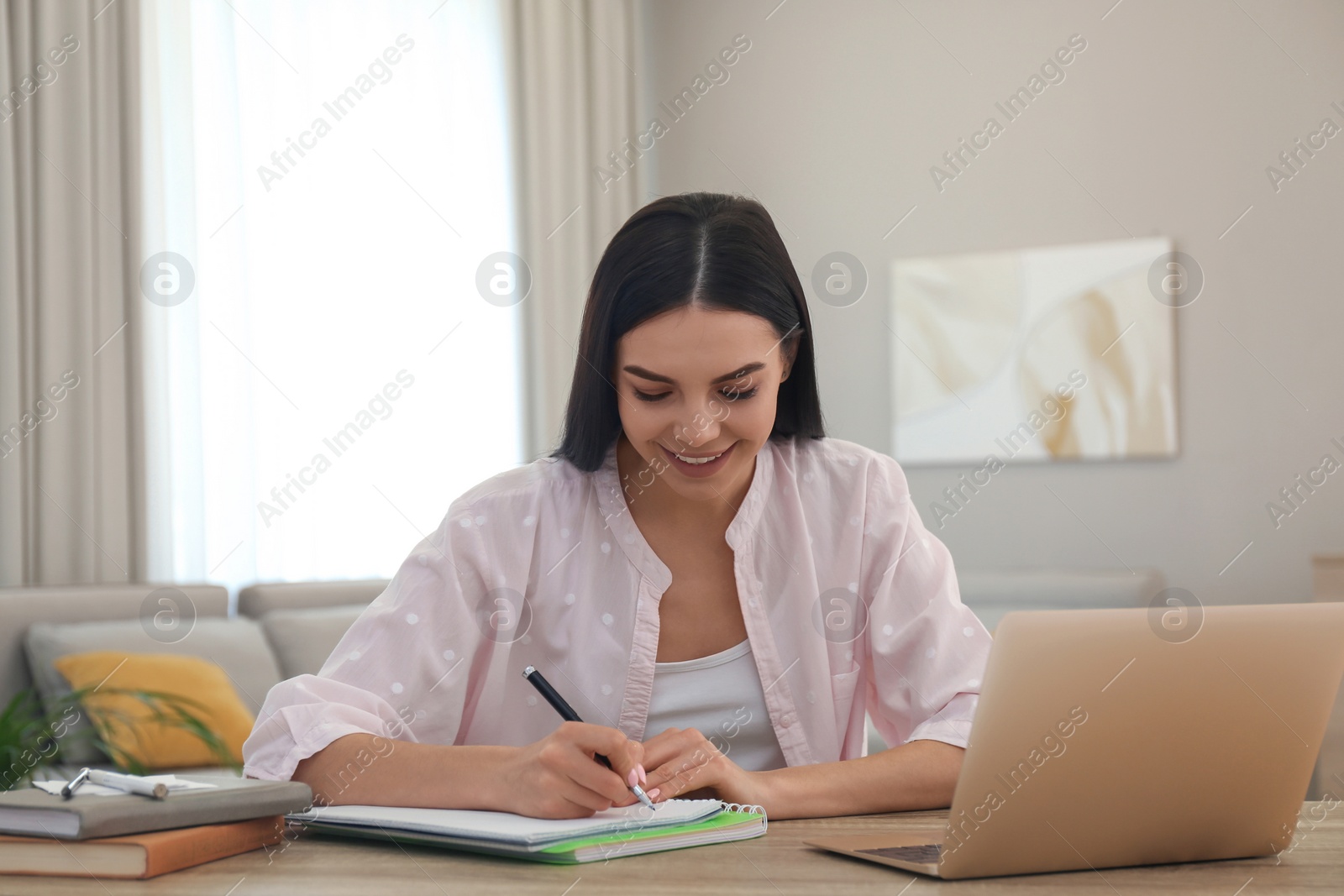 Photo of Young woman taking notes during online webinar at table indoors