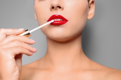 Photo of Beautiful woman applying red gloss on lips against gray background, closeup