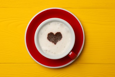 Cup of aromatic coffee with heart shaped decoration on yellow wooden table, top view