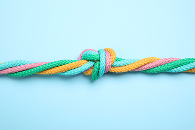 Photo of Colorful ropes tied together on light blue background, top view. Unity concept