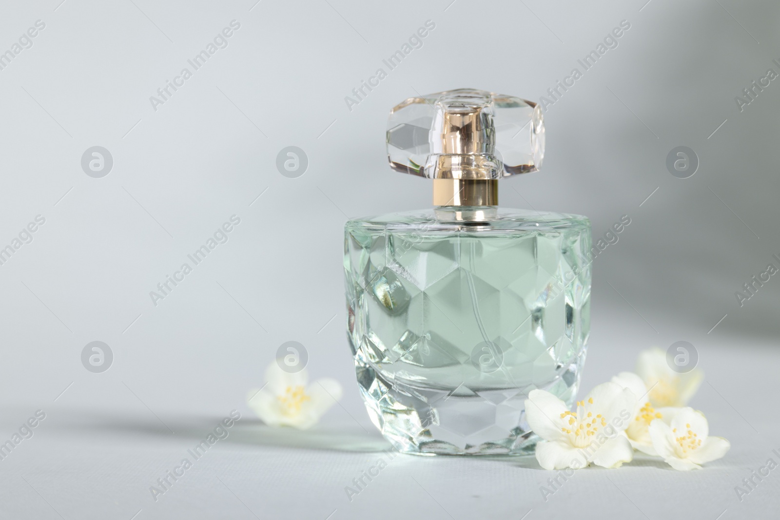 Photo of Aromatic perfume in bottle and beautiful jasmine flowers on grey background, closeup. Space for text