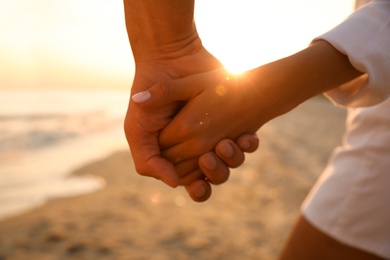 Photo of Lovely couple holding hands on beach at sunset, closeup