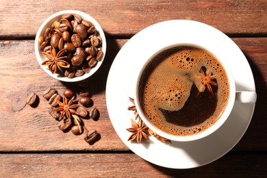 Photo of Aromatic hot coffee with anise stars and beans on wooden table, flat lay