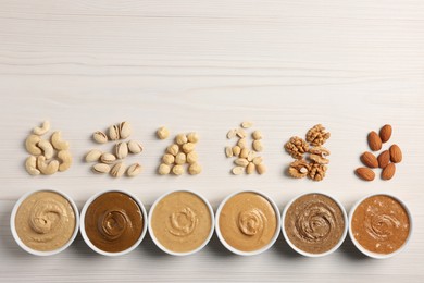 Many tasty nut butters in bowls and nuts on white wooden table, flat lay. Space for text