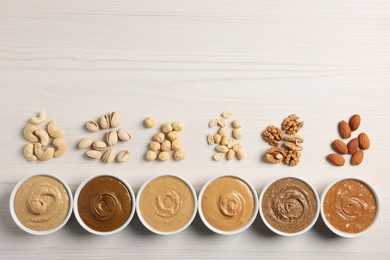 Photo of Many tasty nut butters in bowls and nuts on white wooden table, flat lay. Space for text