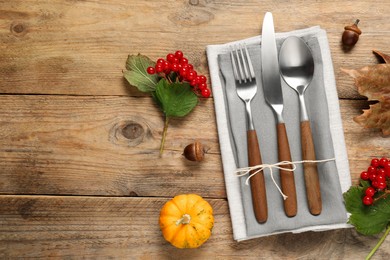 Photo of Autumn table setting. Cutlery, napkins, viburnum berries and pumpkin on wooden background, flat lay with space for text