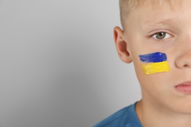 Little boy with drawing of Ukrainian flag on face against light grey background, space for text
