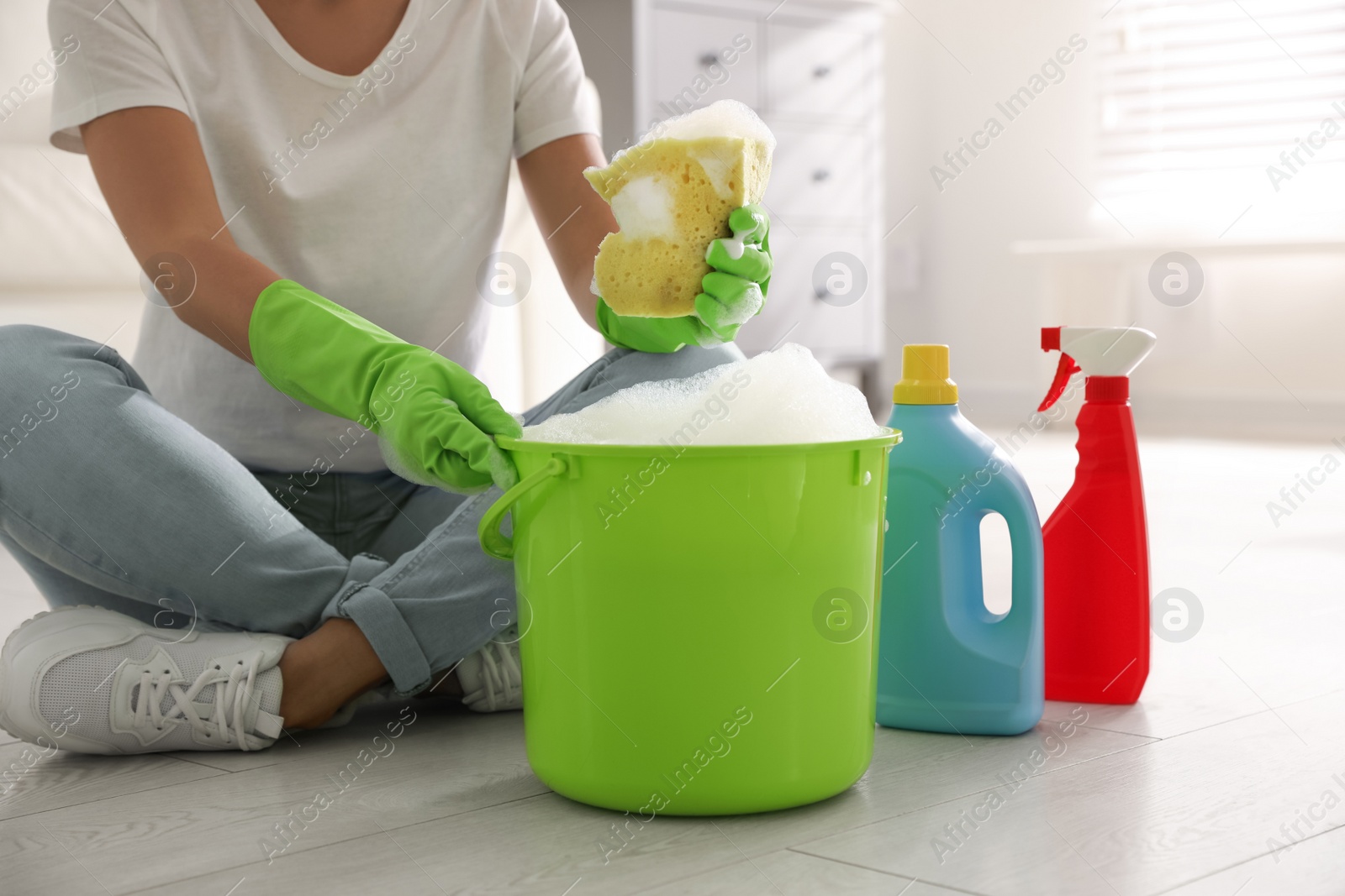 Photo of Woman holding sponge with foam over bucket indoors, closeup. Cleaning supplies