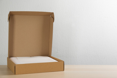 Photo of Open cardboard box on wooden table against light background. Space for text