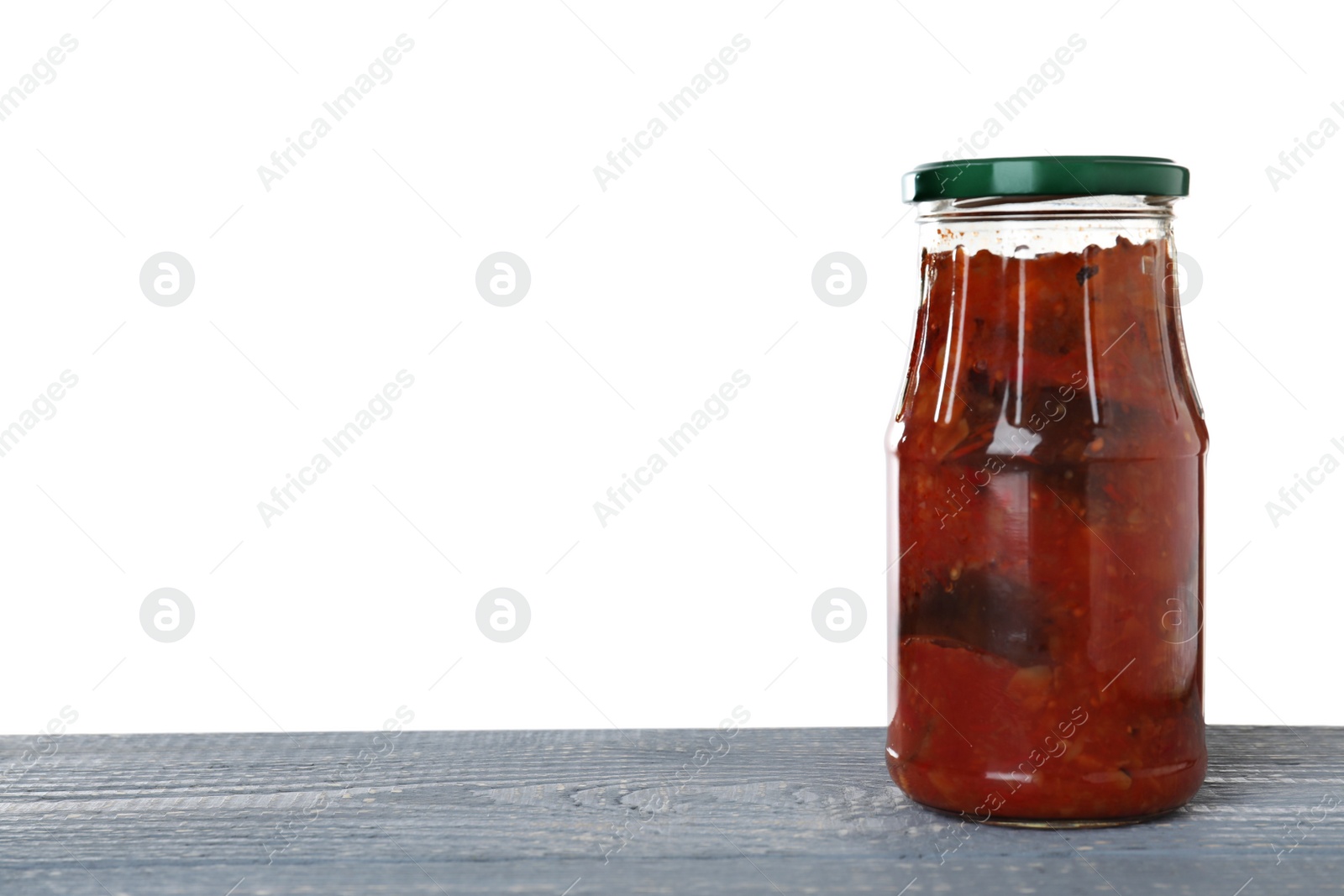 Photo of Jar of vegetable sauce on blue wooden table against white background. Pickled food