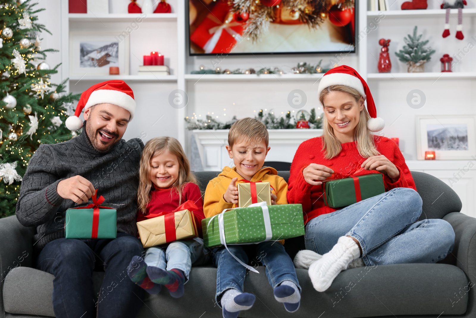 Photo of Happy family in Santa hats with Christmas gifts on sofa at home