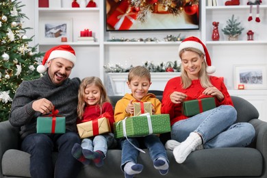 Happy family in Santa hats with Christmas gifts on sofa at home