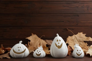 Photo of Jack-o-Lantern holders and autumn leaves on table against wooden background, space for text. Halloween decor