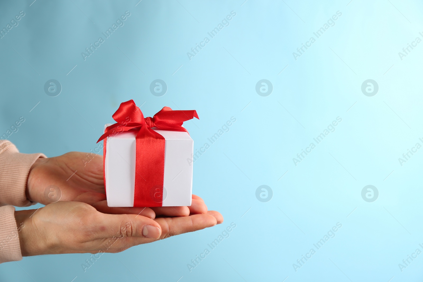 Photo of Woman holding gift box on light blue background,  space for text. Valentine's Day celebration