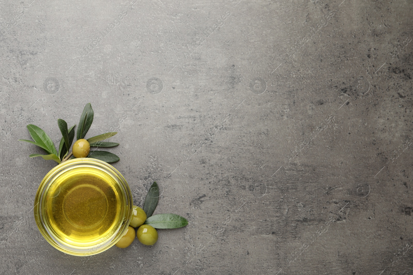 Photo of Glass bowl of oil, ripe olives and green leaves on grey table, flat lay. Space for text