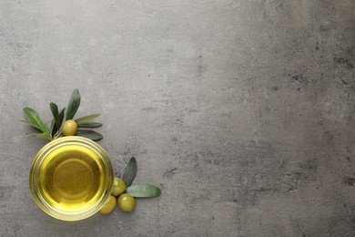 Photo of Glass bowl of oil, ripe olives and green leaves on grey table, flat lay. Space for text