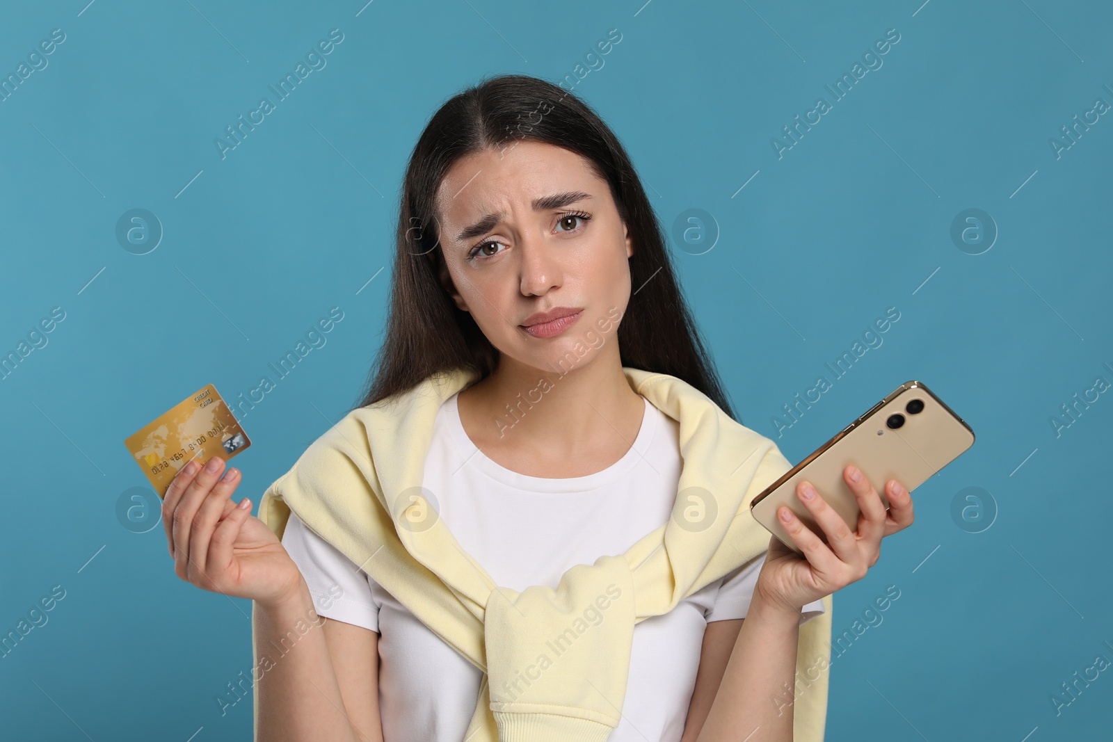 Photo of Confused woman with credit card and smartphone on light blue background. Debt problem