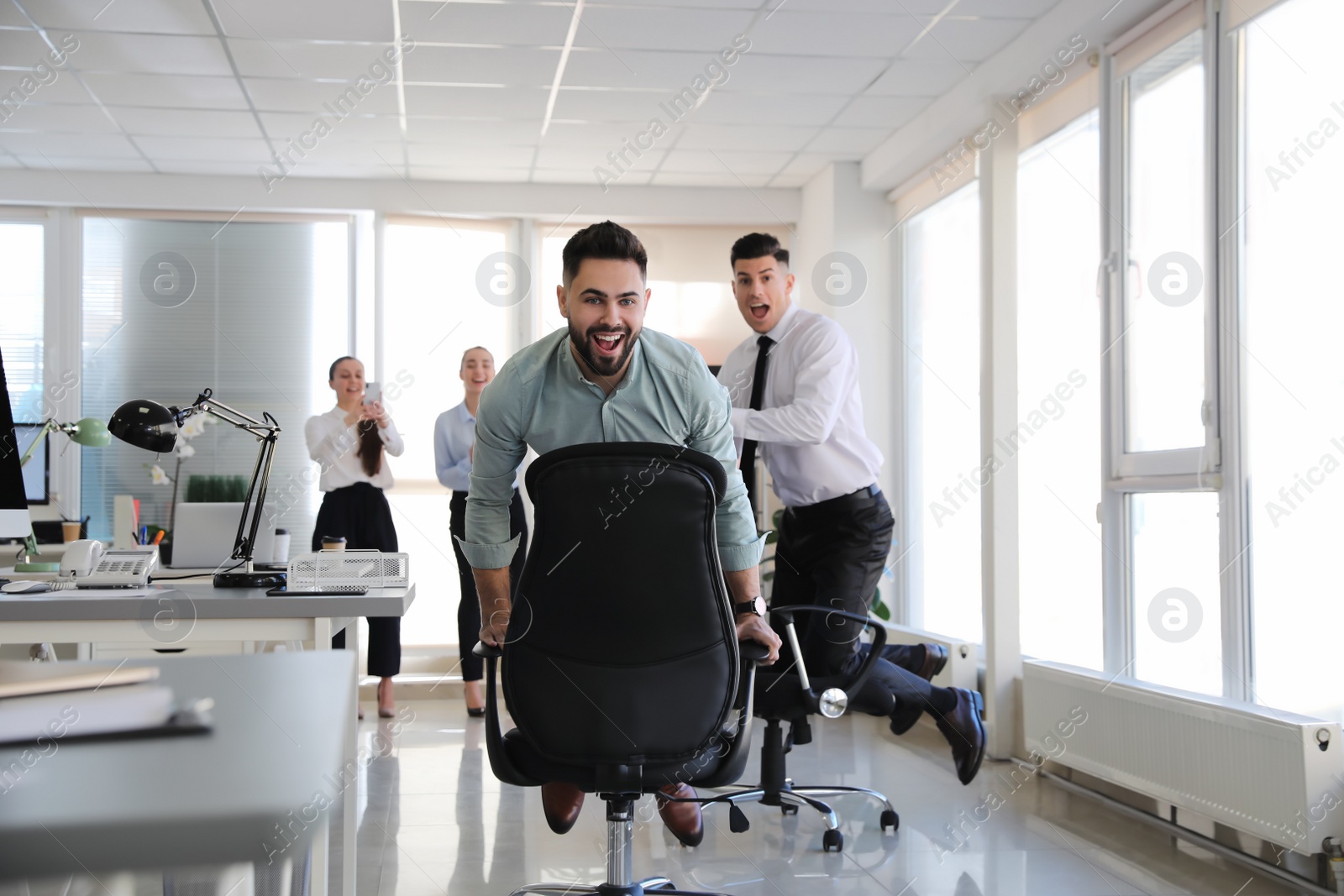 Photo of Happy office employees riding chairs at workplace