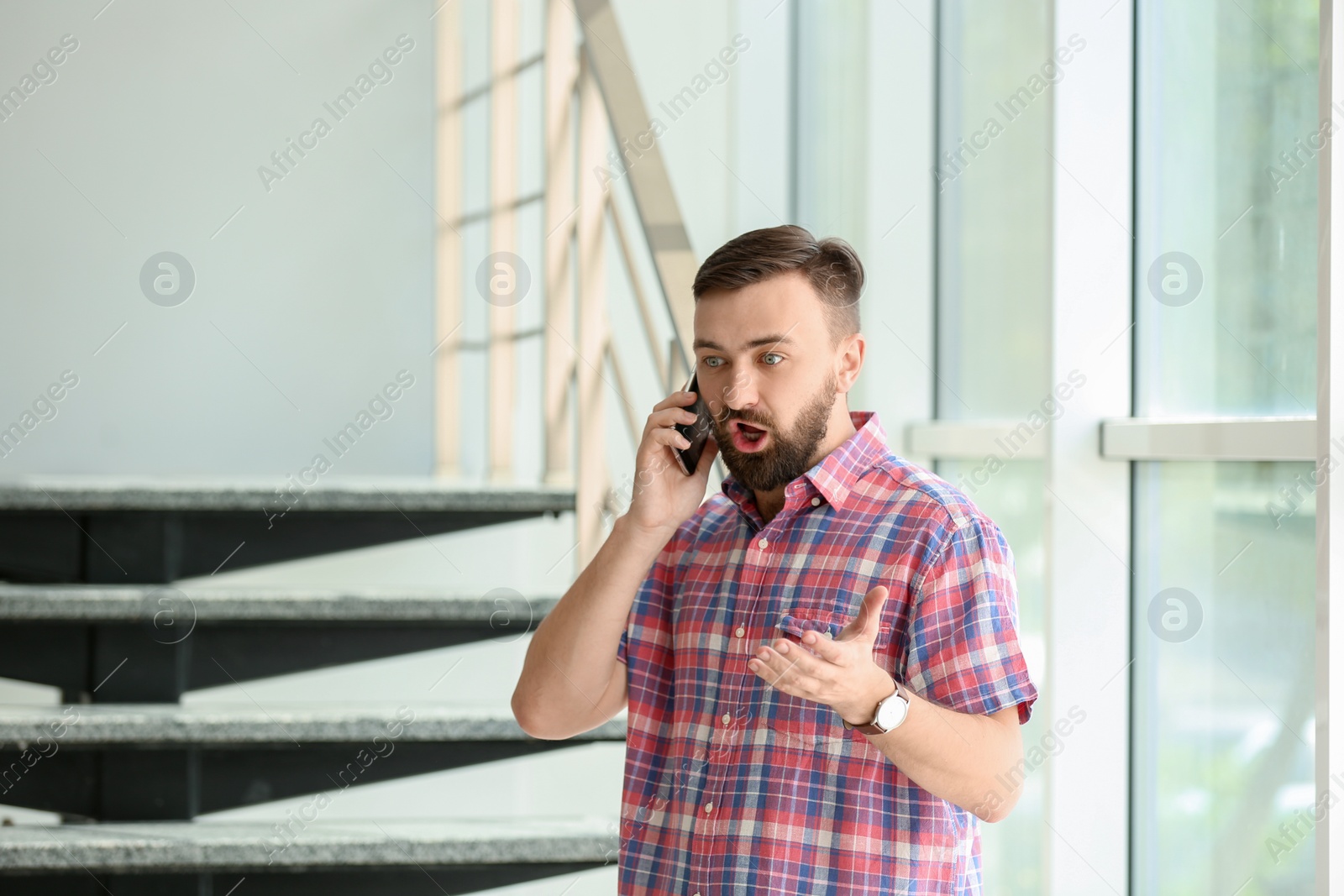 Photo of Portrait of handsome bearded man with mobile phone near stairs, indoors