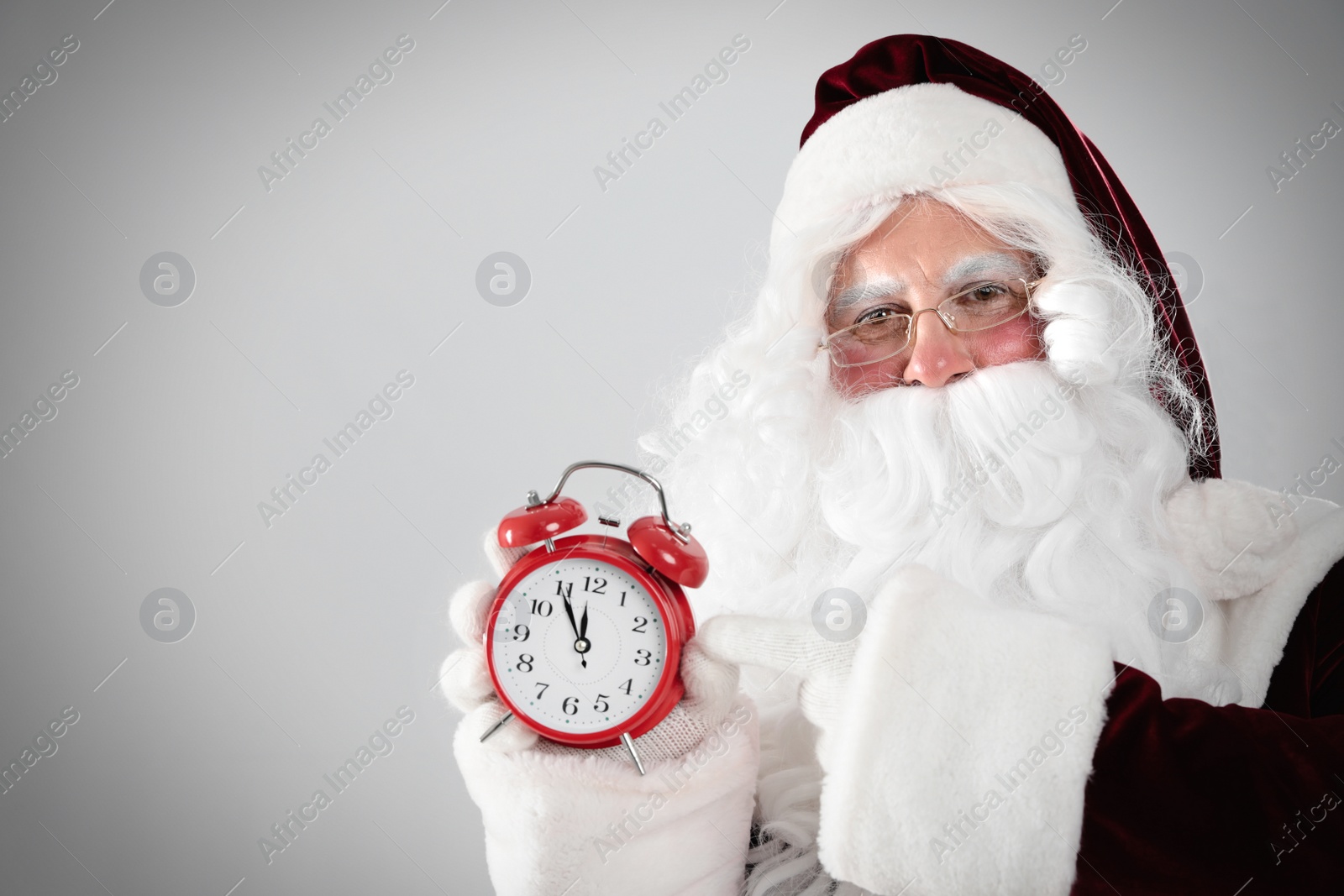 Photo of Santa Claus holding alarm clock on light grey background, space for text. Christmas countdown