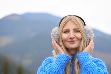 Photo of Young beautiful woman wearing warm earmuffs in mountains