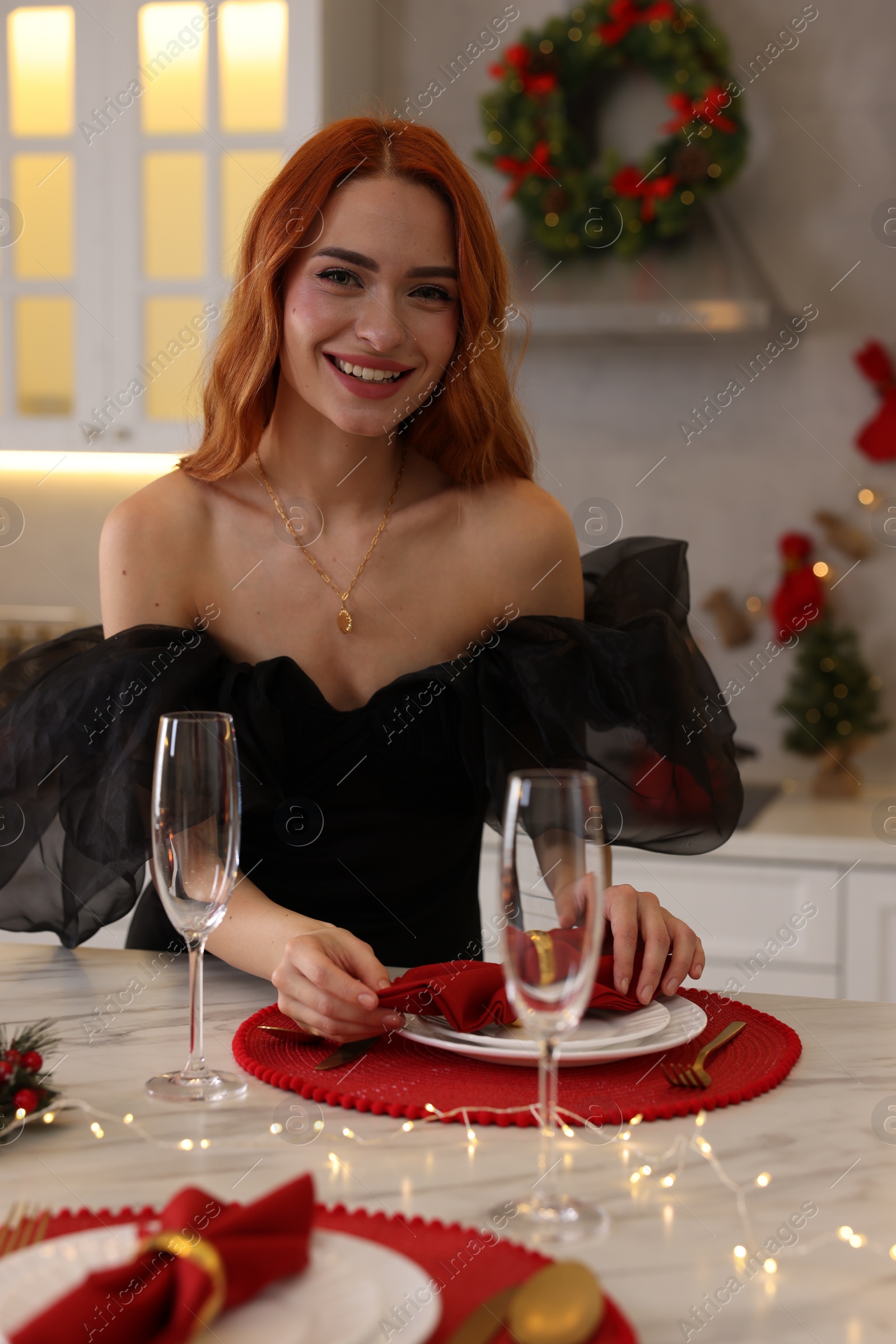 Photo of Beautiful young woman setting table for Christmas celebration in kitchen