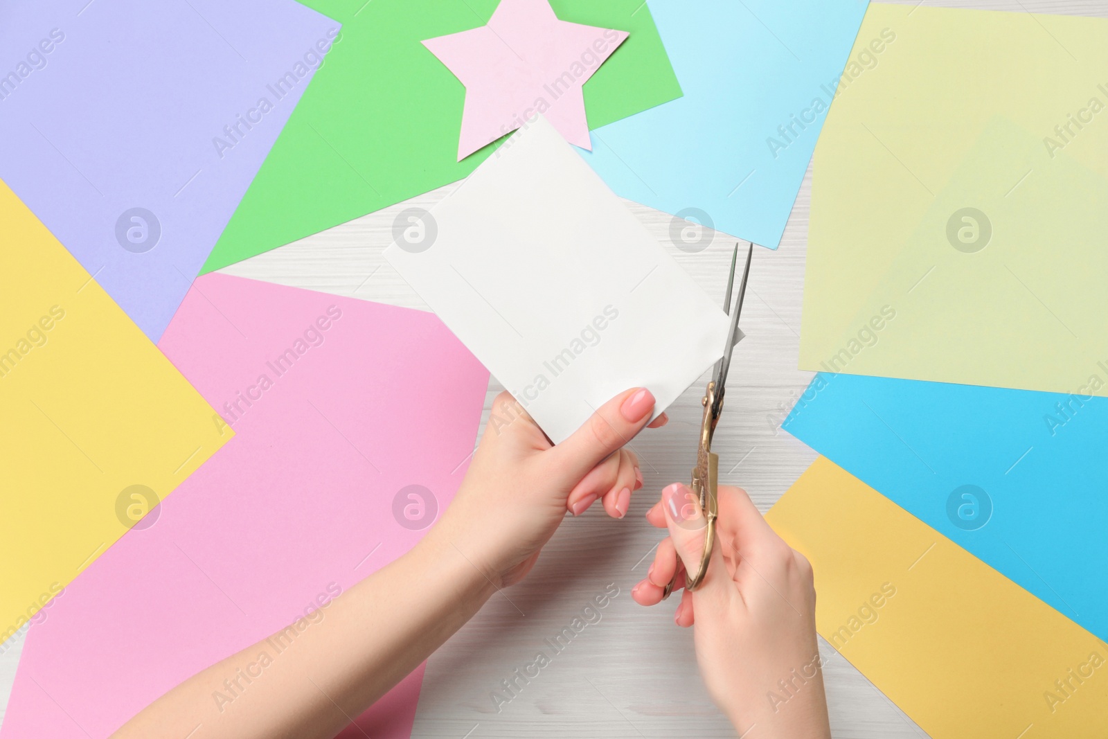 Photo of Woman cutting paper with scissors at white wooden table, top view